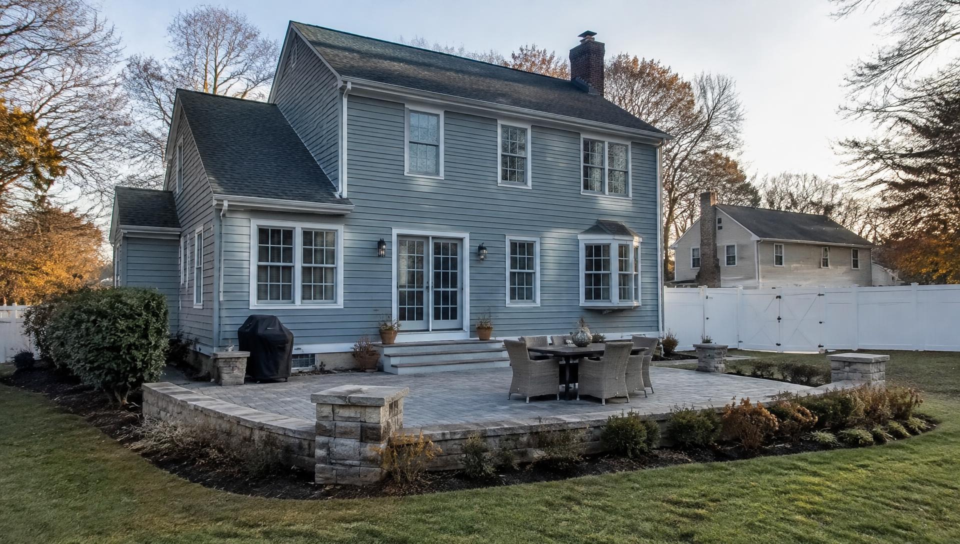 Finished paver patio with stone seat wall behind a New England colonial home